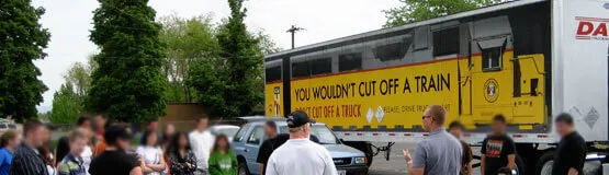 Group gathered near a semi-truck trailer reading You Wouldn't Cut Off a Train